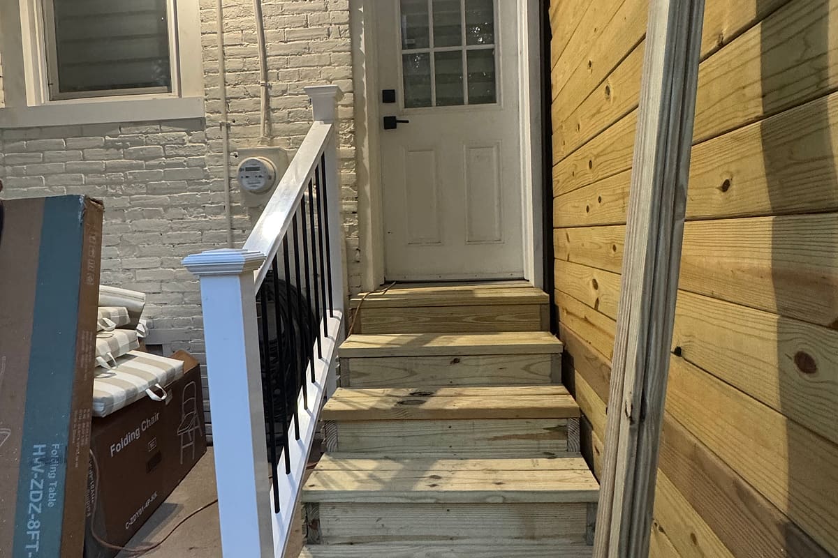 New wood privacy fence with deck stairs and a black railing at a back door